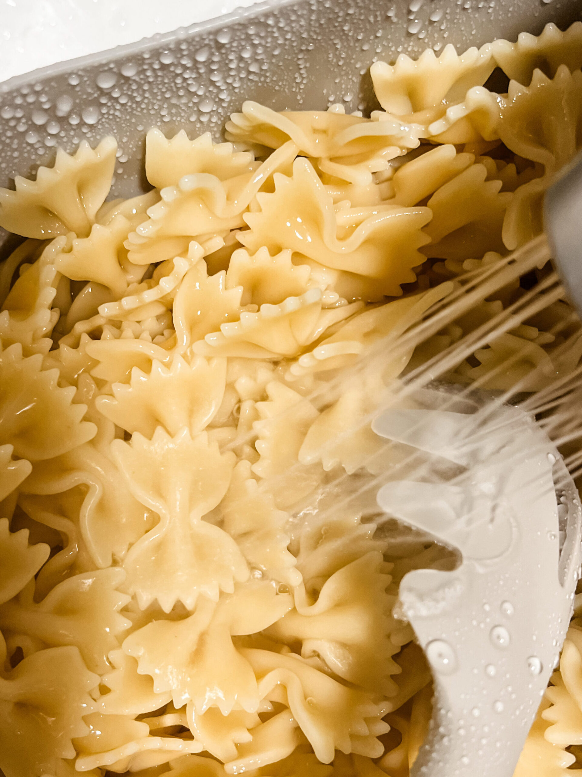 Bow tie pasta noodles being strained and rinsed in cold water