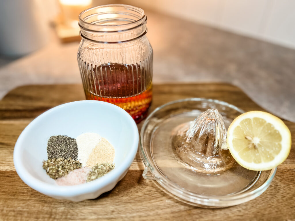 Salad dressing ingredients, seasonings in a bowl next to lemon juicer with lemon half and a mason jar with oil and vinegar