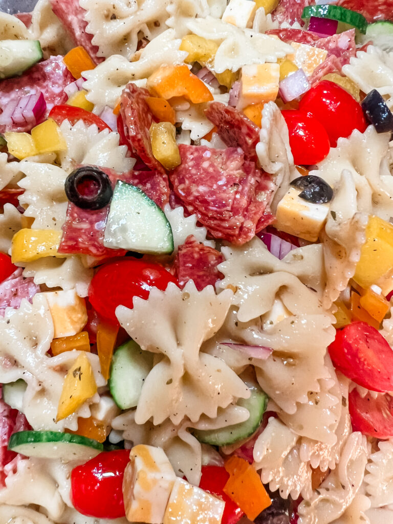 Bow tie pasta noodles with olives, pepperoni, cucumbers, bell peppers, cheeses, tomatoes, and red onion.